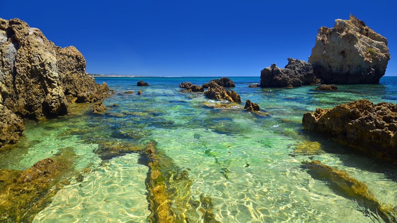 1415014879 View of the spectacular beach of Arrifes, Albufeira, one of the most beautiful beaches of the Portuguese Algarve, with its imposing cliffs and golden rock formations and its transparent waters, ideal for all kinds of water activities such as snorkeling, kayaking, diving